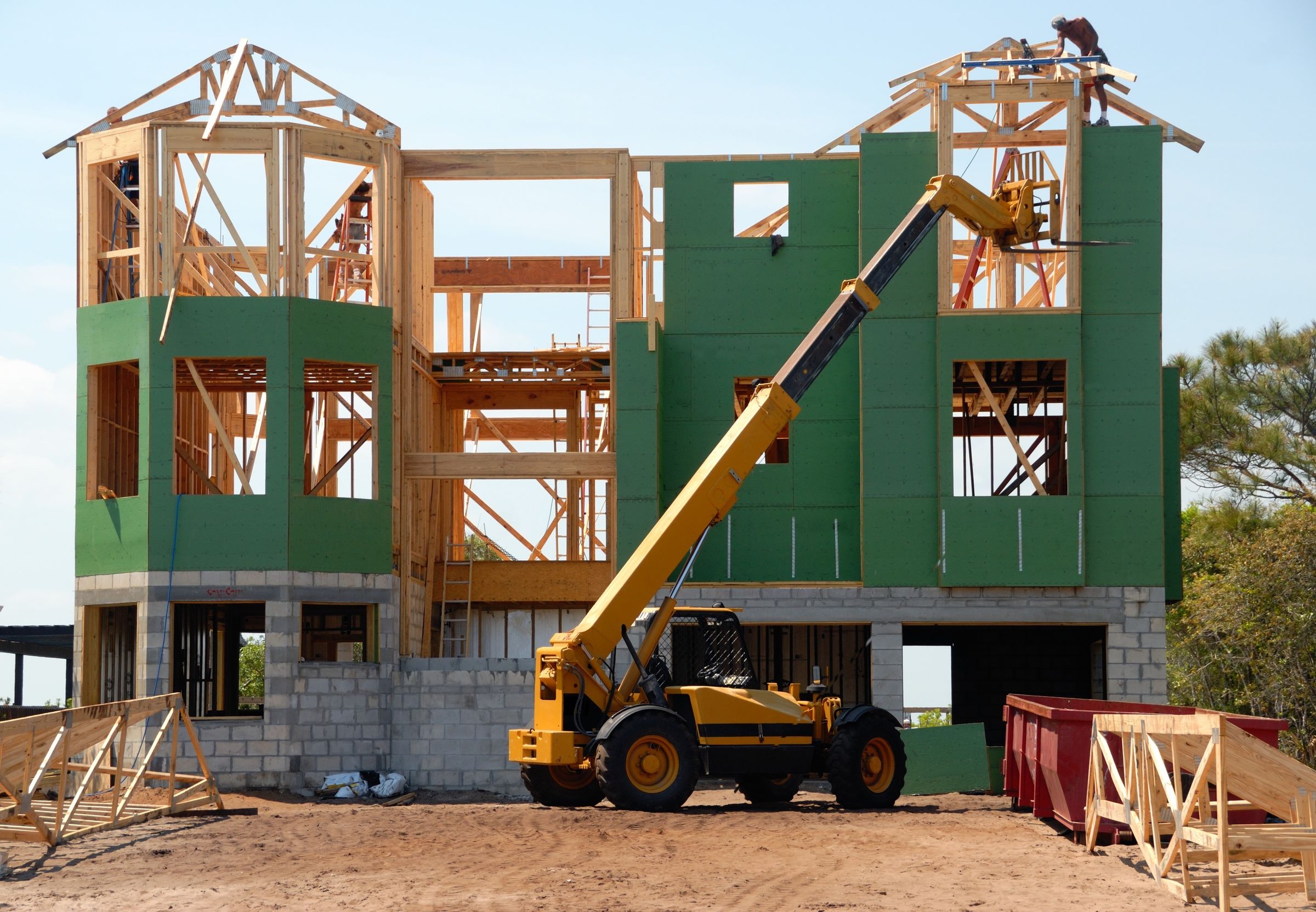 House framing on a sunny jobsite with a yellow telehandler and a worker on the roof. Photo by Pixabay on Pexels.