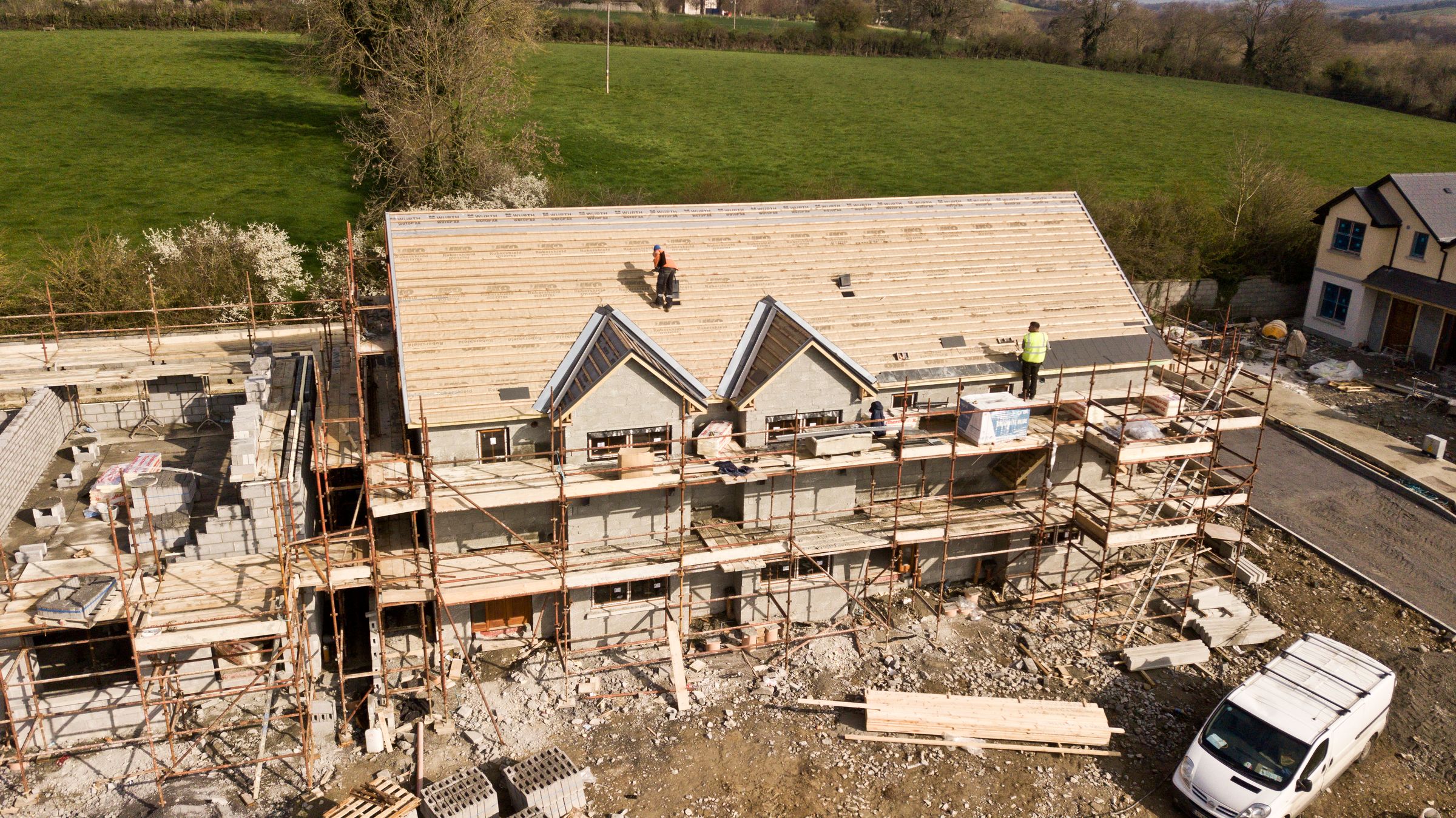 Aerial view of a house under construction with roofers on the decking and scaffolding around the walls. Photo by Steffen Coonan on Pexels.